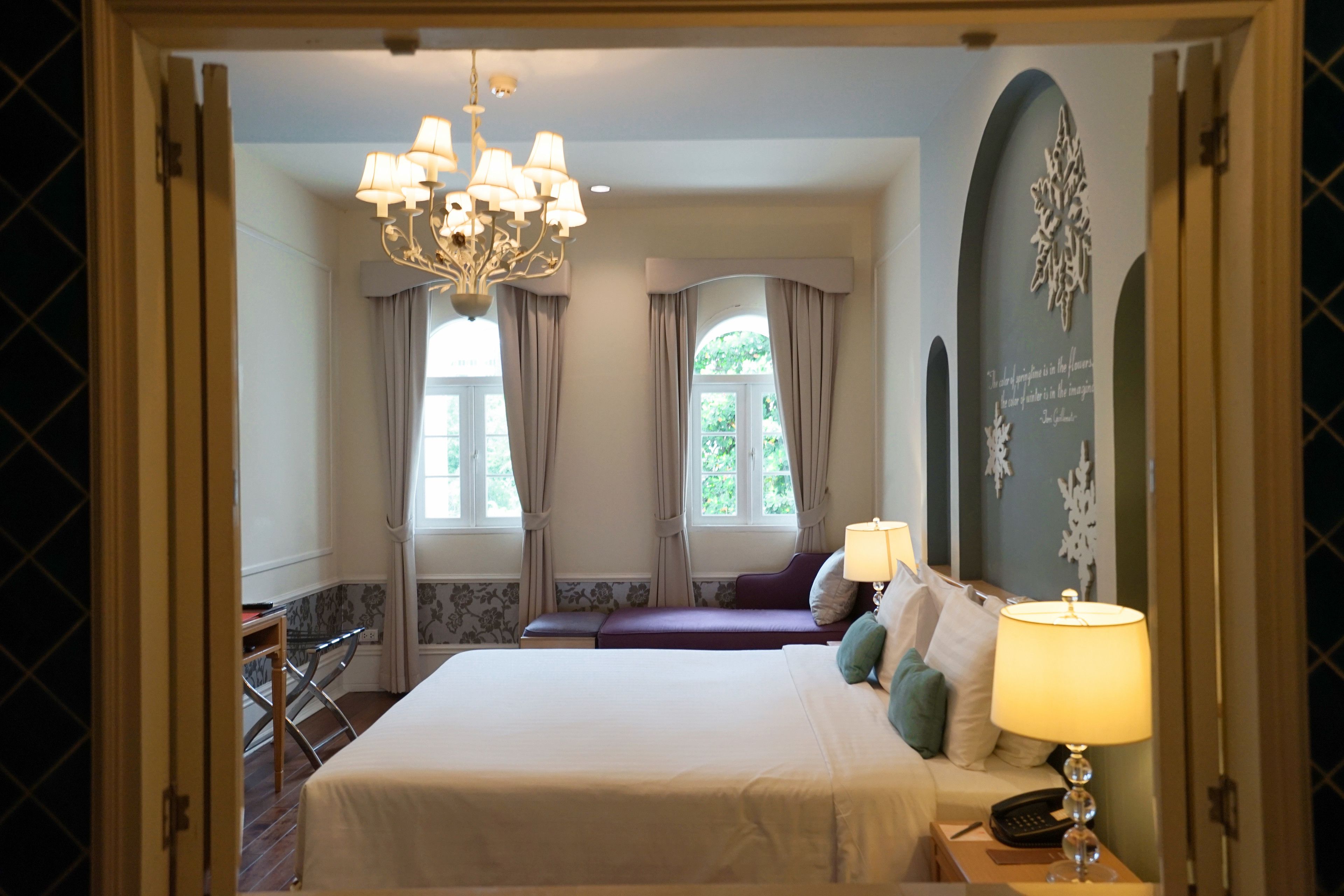 Ein Schlafzimmer mit einem großen Bett, einem Nachttisch mit Lampe, einer Bank und Blick ins Freie durch ein Fenster.