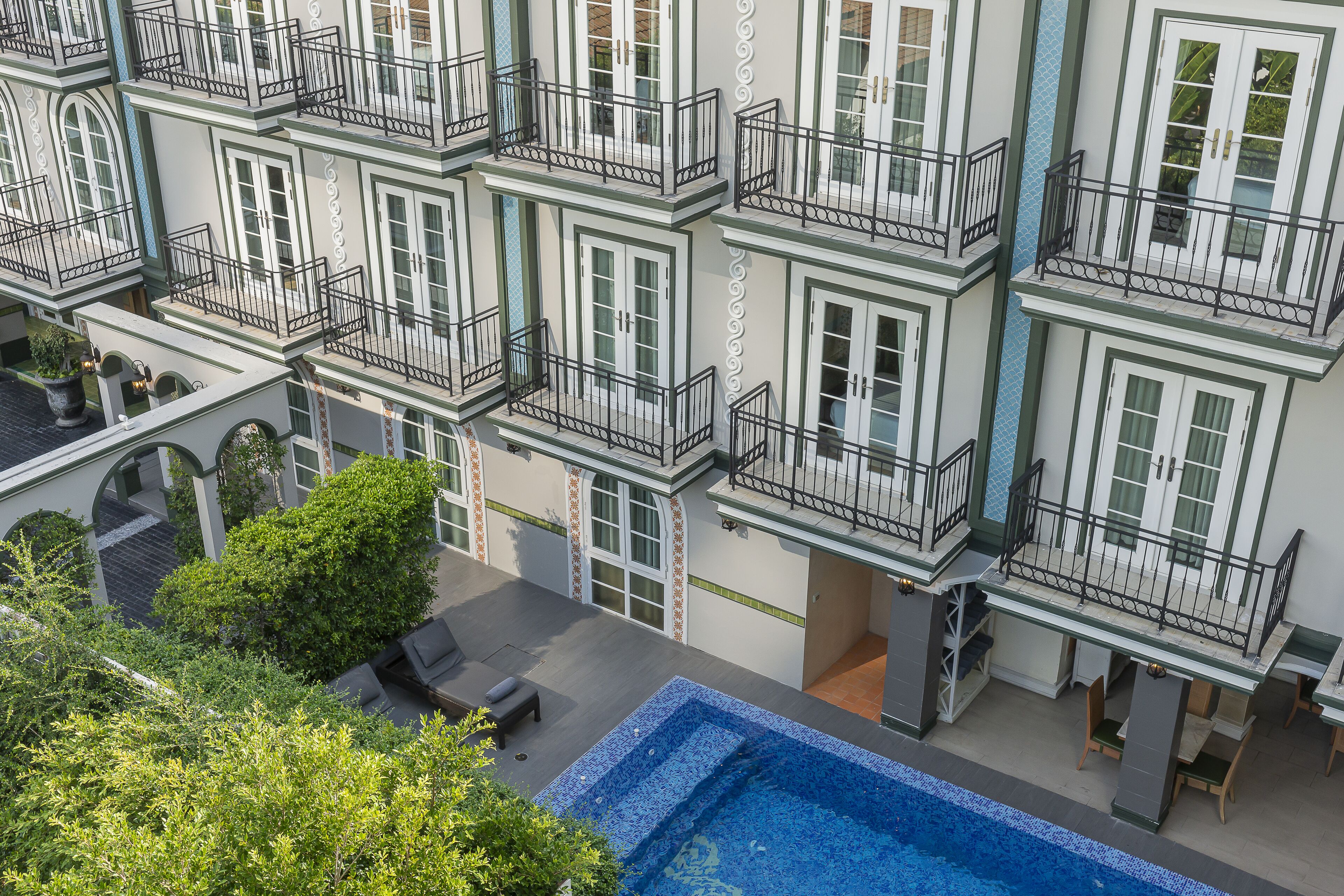Un hotel de varios pisos con balcones, piscina y asientos al aire libre.