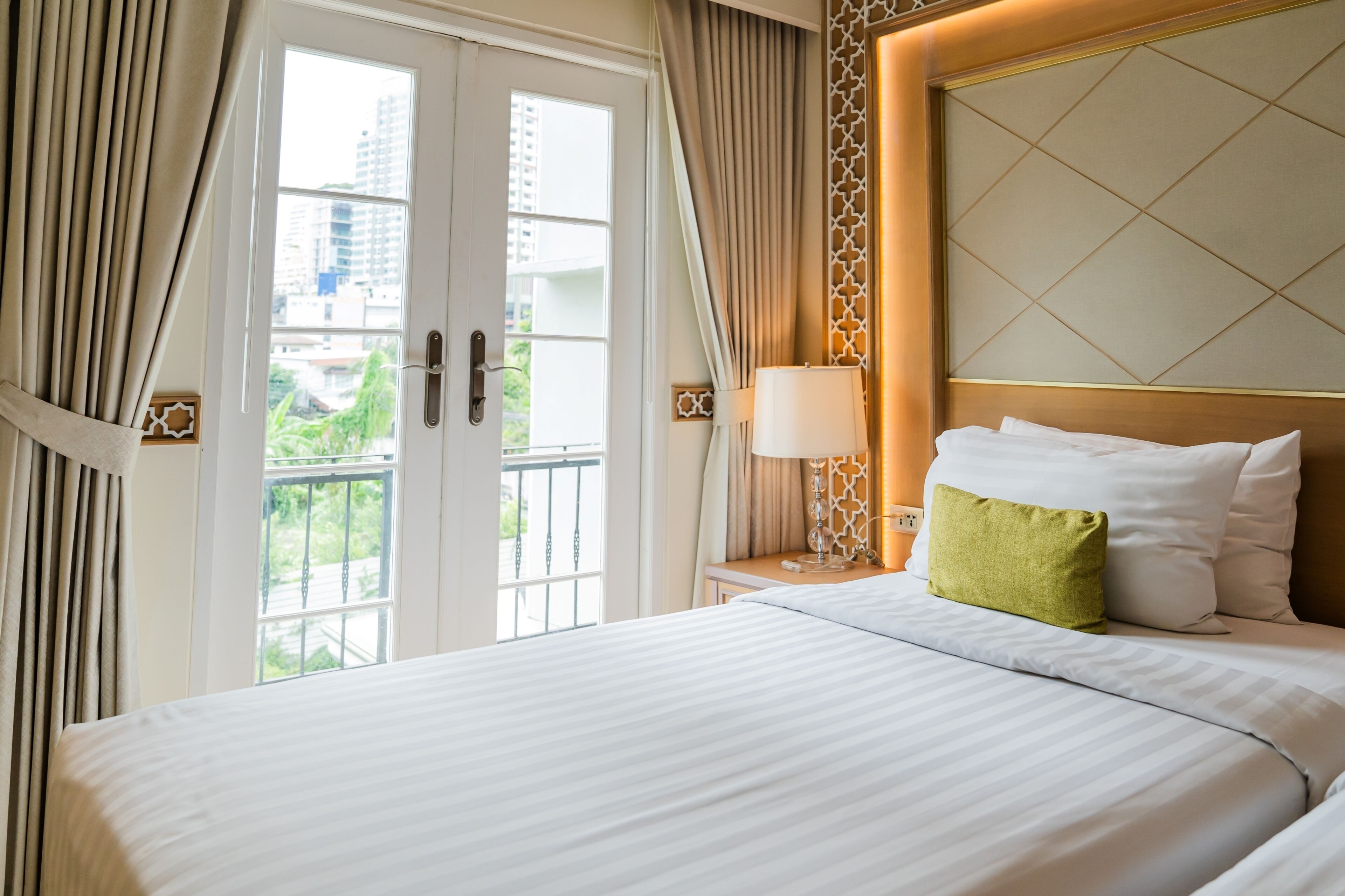 A hotel room with a large bed, a nightstand with a lamp, and a view of the outdoors through a glass door.