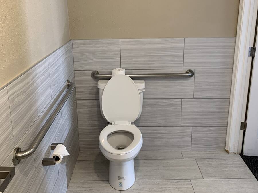 Une salle de bain moderne avec des toilettes blanches, des barres d'appui et un sol carrelé.
