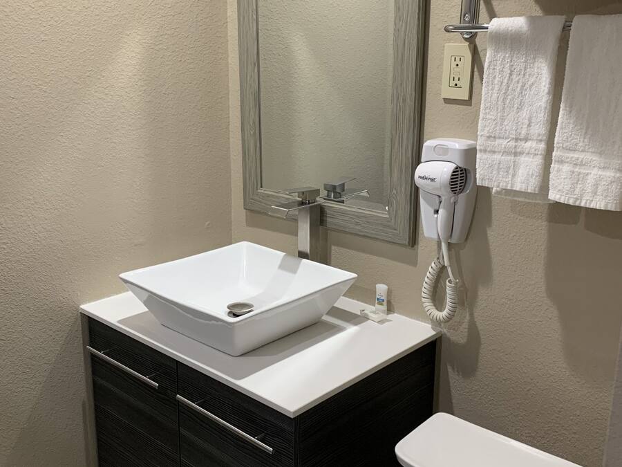 A bathroom with a white sink, dark wooden vanity, a mirror, a towel rack, and a hairdryer.
