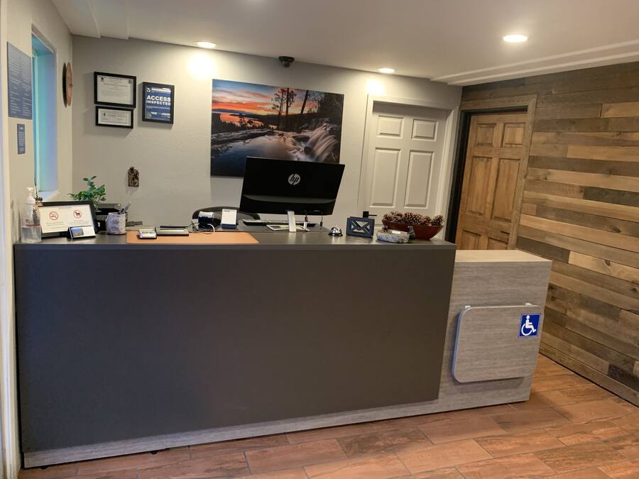 A reception desk with a computer, framed certificates, a clock, and a painting of a landscape.