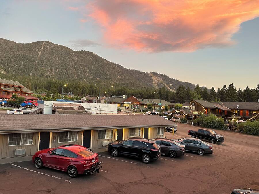 A parking lot with several cars, a building with a sign that reads "BBQ", and a mountain in the background.