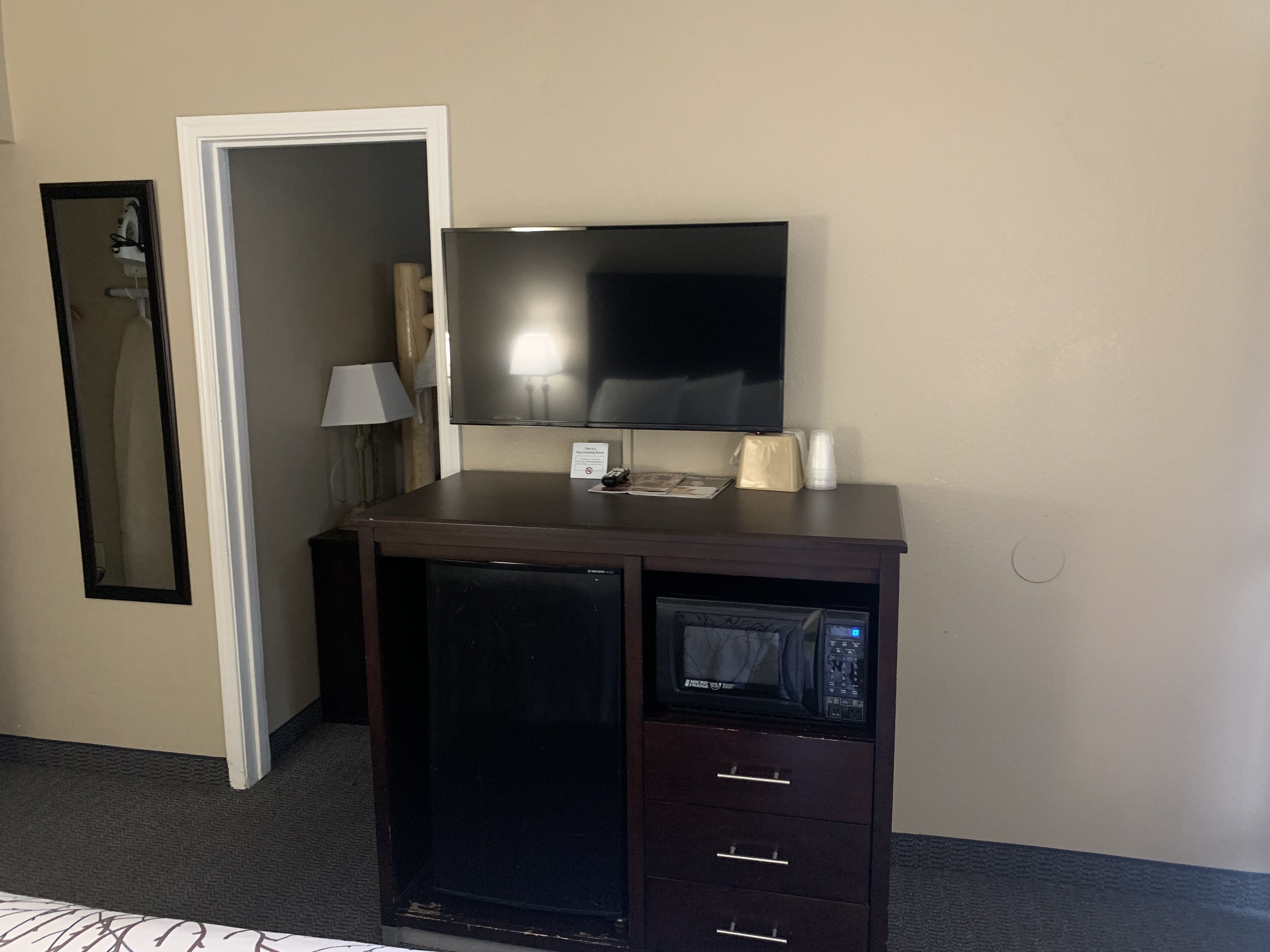 Una camera d'albergo compatta con una TV a schermo piatto montata su un mobile in legno, un forno a microonde e un piccolo frigorifero.