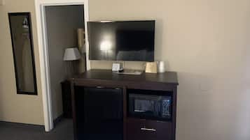 Una camera d'albergo compatta con una TV a schermo piatto montata su un mobile in legno, un forno a microonde e un piccolo frigorifero.