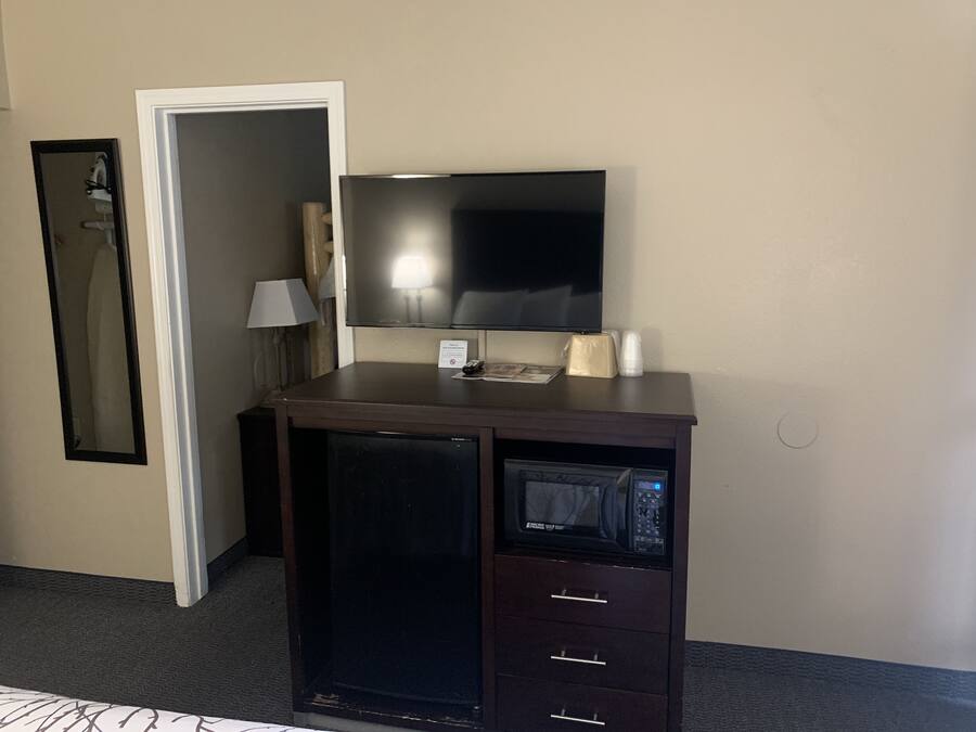Una camera d'albergo compatta con una TV a schermo piatto montata su un mobile in legno, un forno a microonde e un piccolo frigorifero.