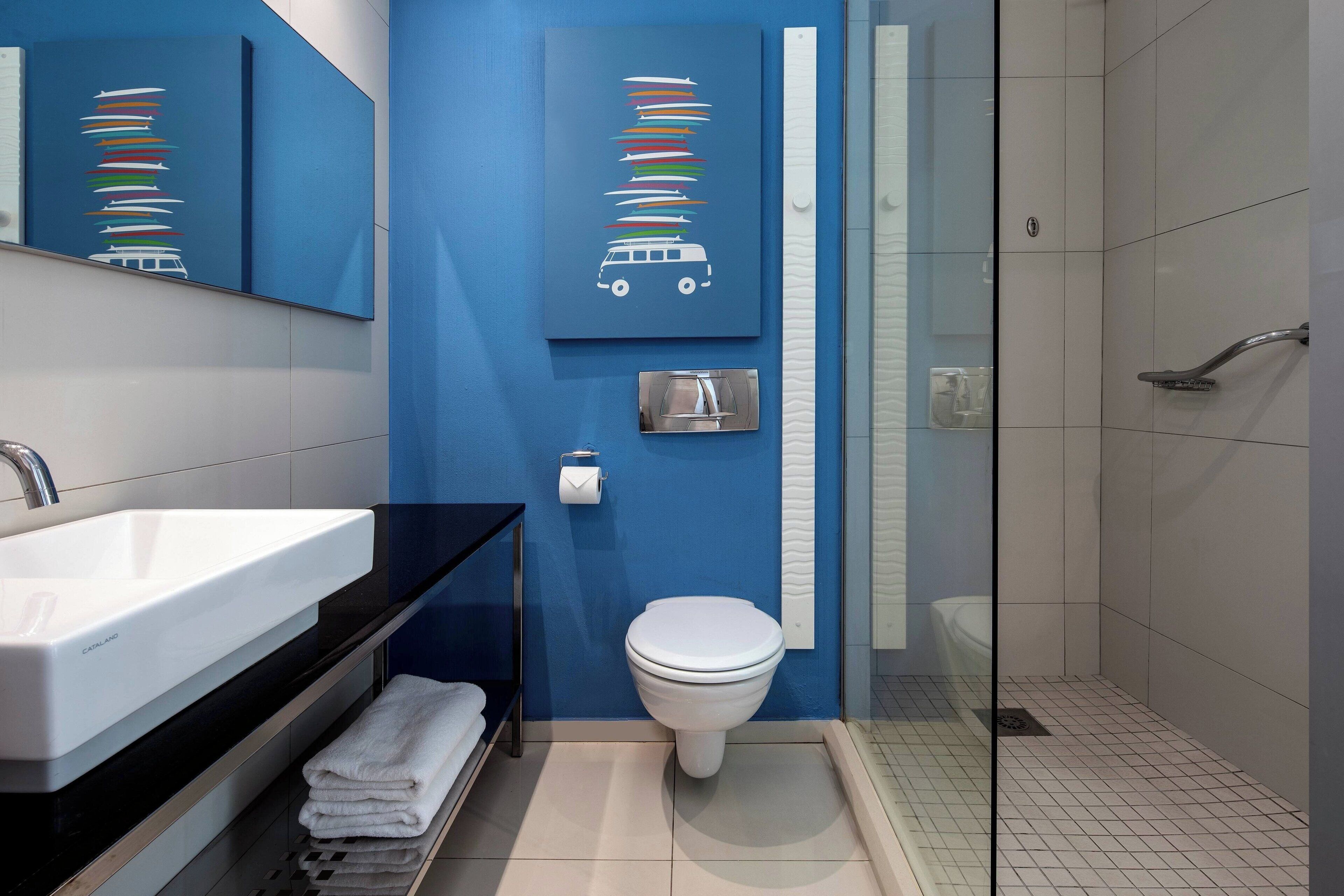 Uma casa de banho moderna com parede azul de destaque, sanita branca, lavatório preto e cabine de duche em vidro.
