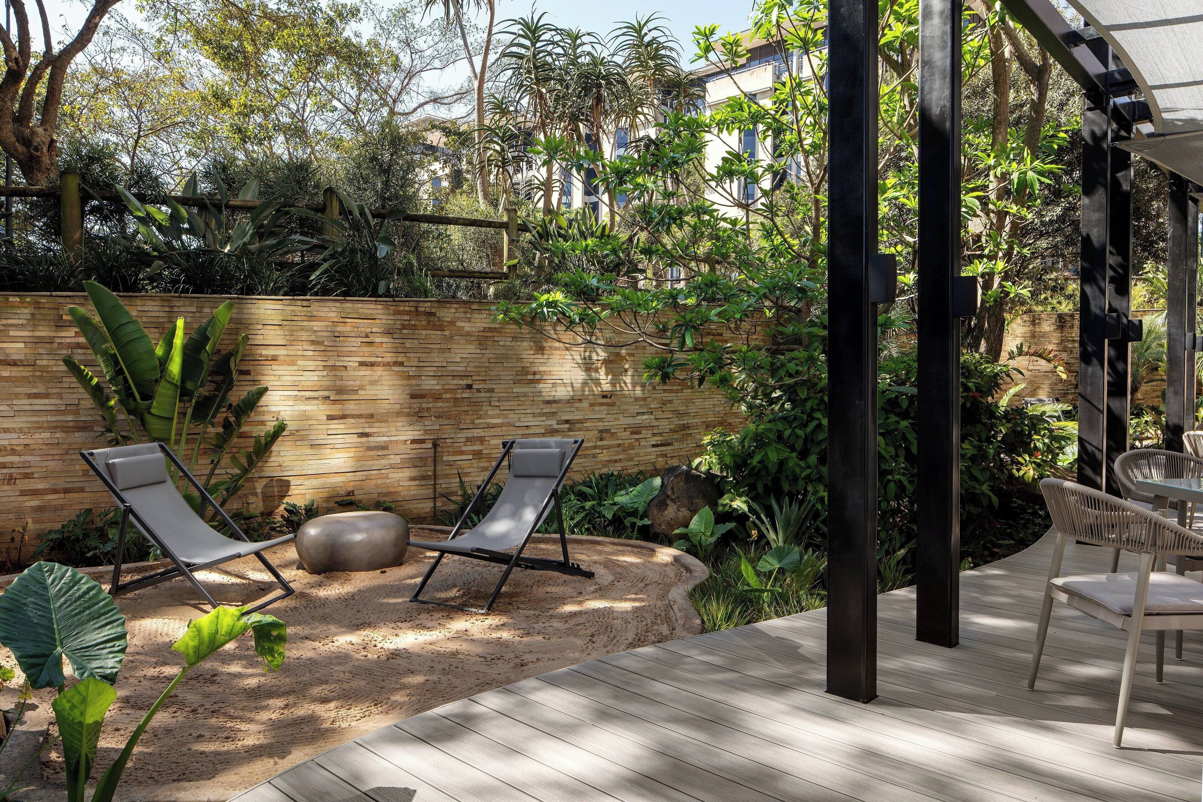 A patio area with two lounge chairs, a wooden deck, and a brick wall.
