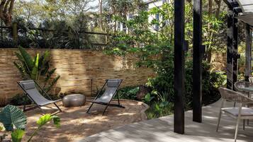 A patio area with two lounge chairs, a wooden deck, and a brick wall.