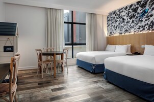Una habitación de hotel con dos camas, una mesa de comedor con sillas, un ventanal con cortinas y una obra de arte colgada en la pared.