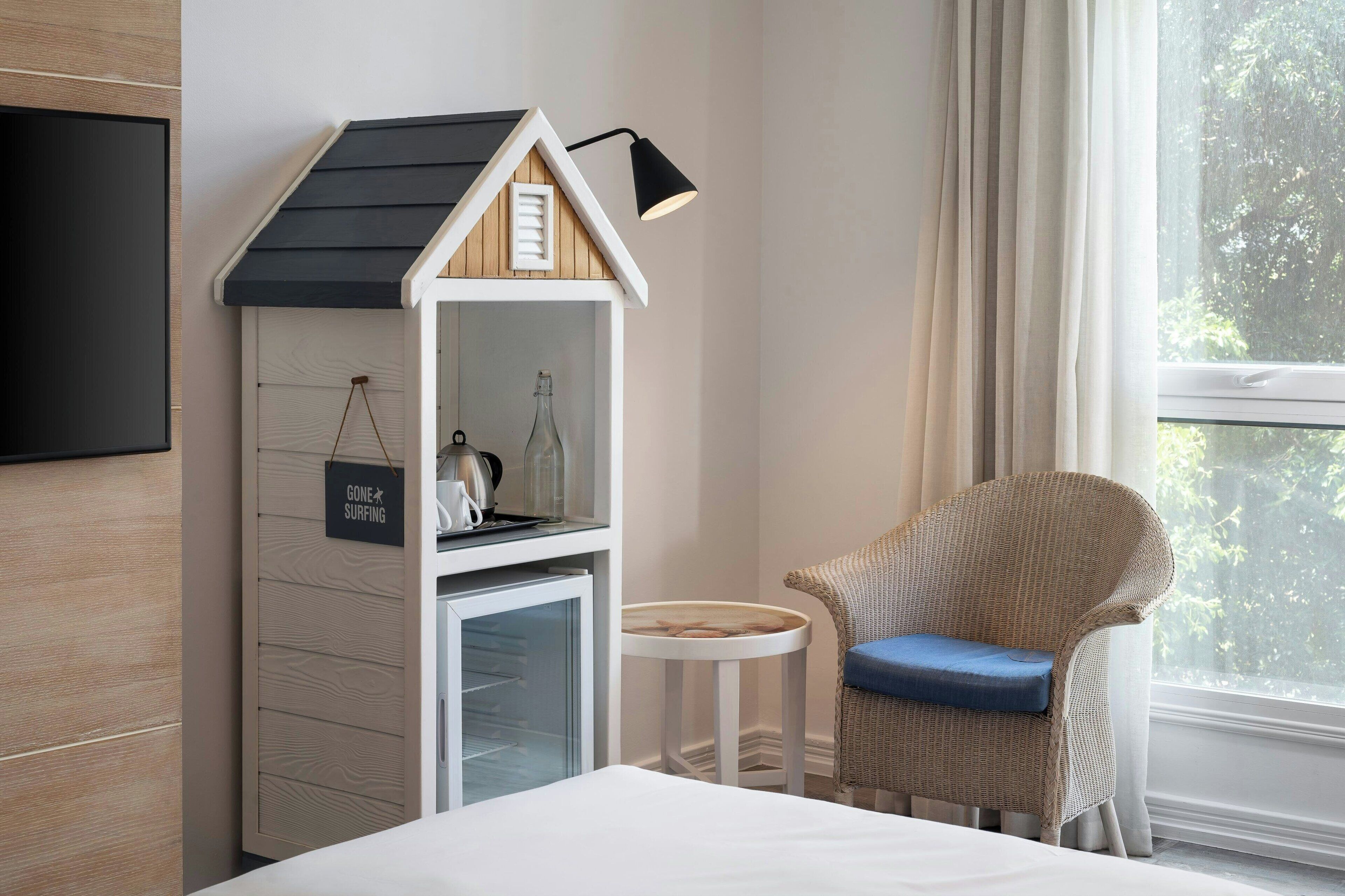 Una habitación de hotel con una casita de juegos, una silla de mimbre, una mesita y una cama.