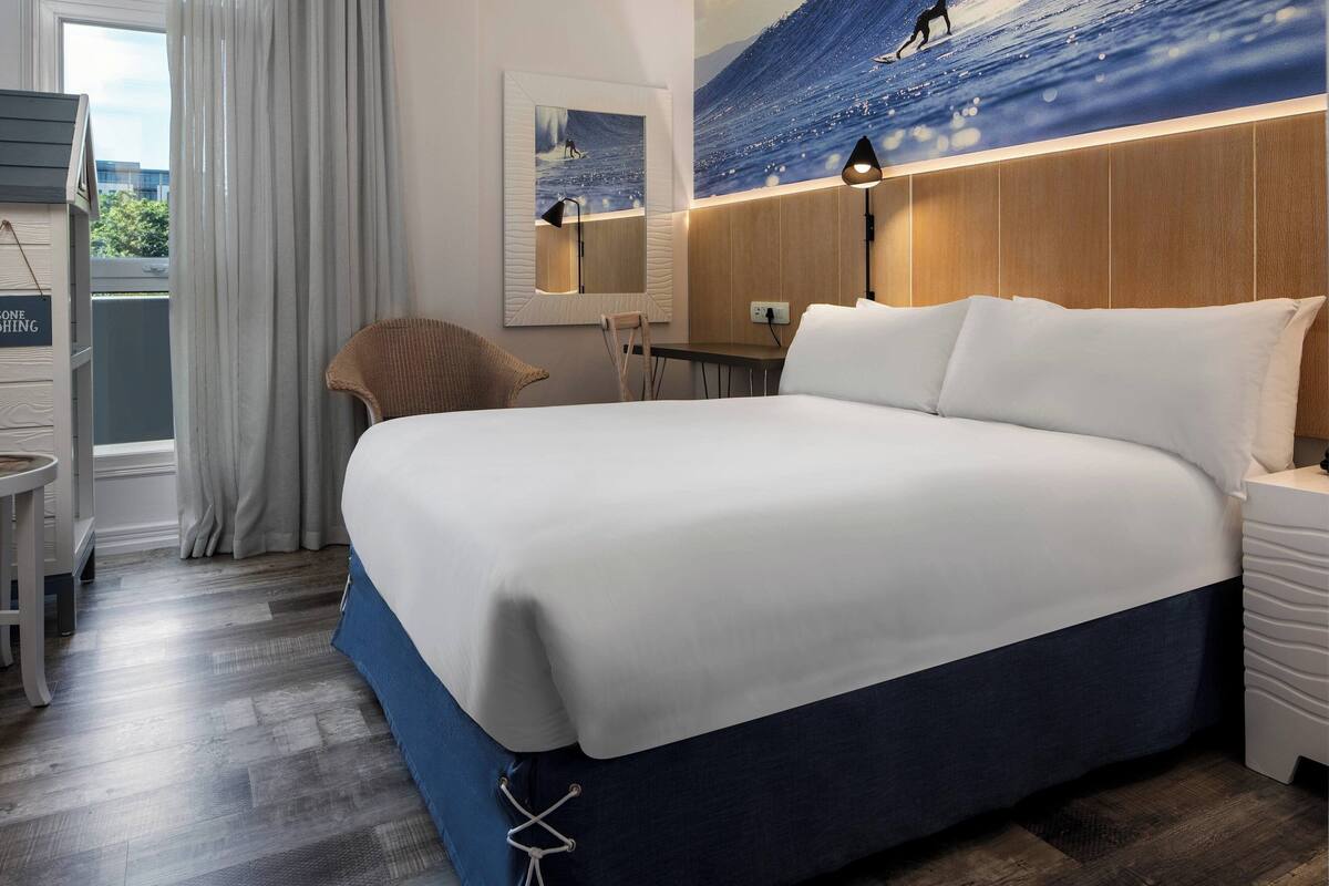 Habitació d'hotel amb un llit gran, una taula de treball, una cadira i vista a l'oceà per la finestra.