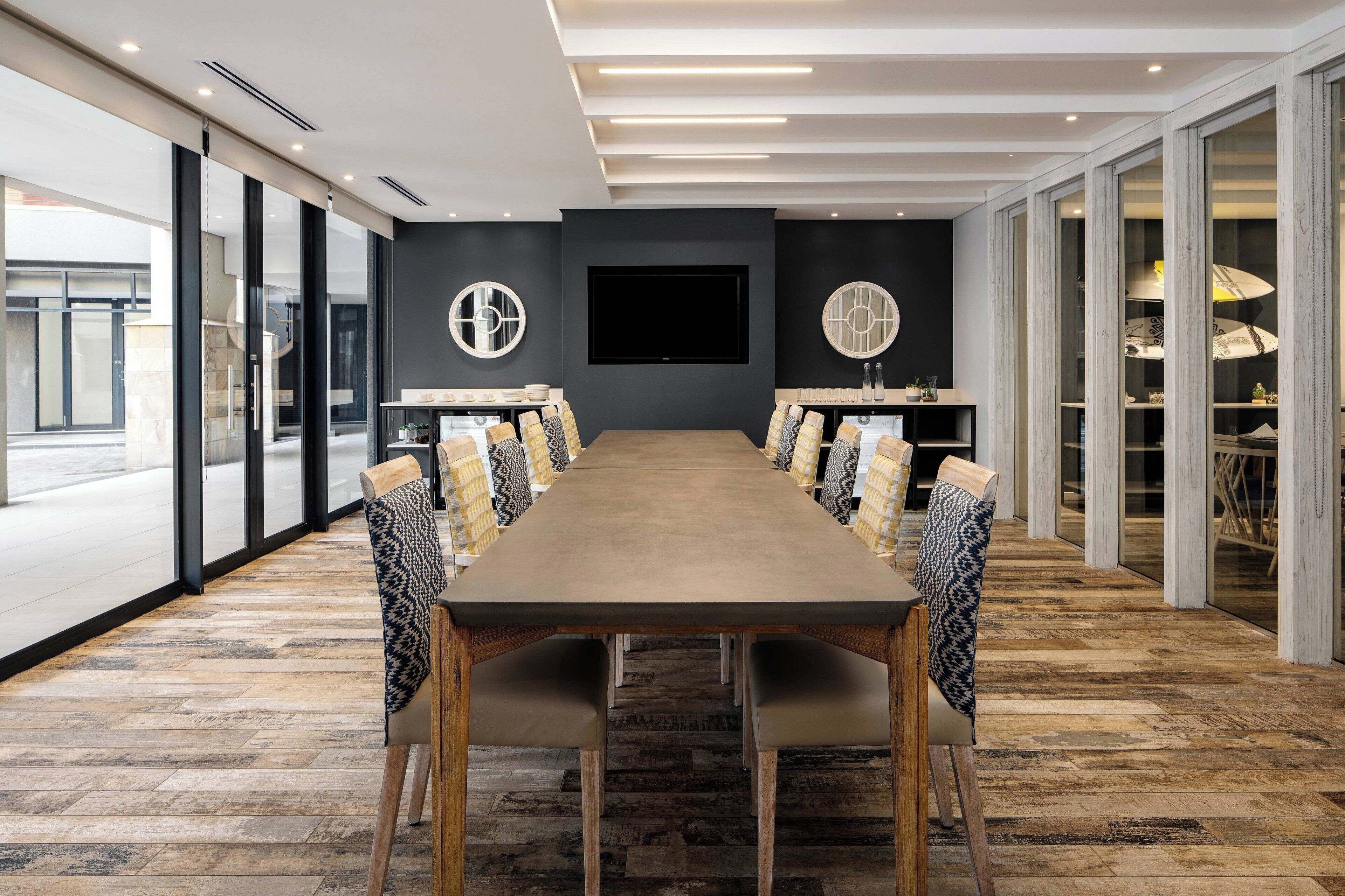 A conference room with a long table, chairs, and a large screen.