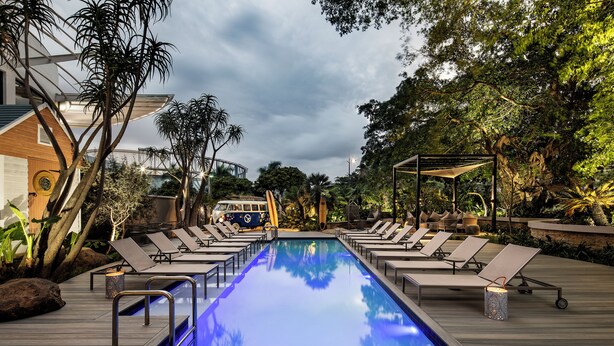 Uma área de piscina com espreguiçadeiras, piscina e vegetação ao redor.
