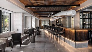 Uma área de bar moderna com um balcão comprido, banquetas e um teto alto com vigas de madeira.