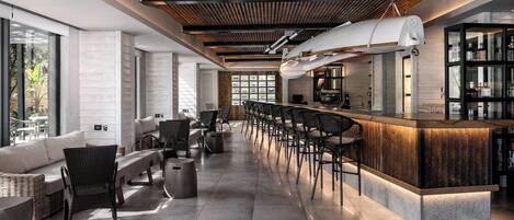 A modern bar area with a long counter, bar stools, and a high ceiling with wooden beams.