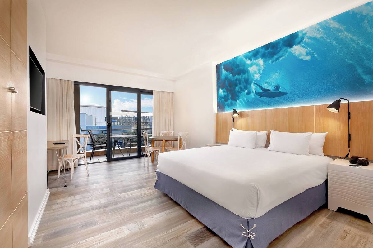 Una habitació d'hotel moderna amb un llit gran, una taula de treball i una cadira. Es veu un paisatge urbà per la finestra.
