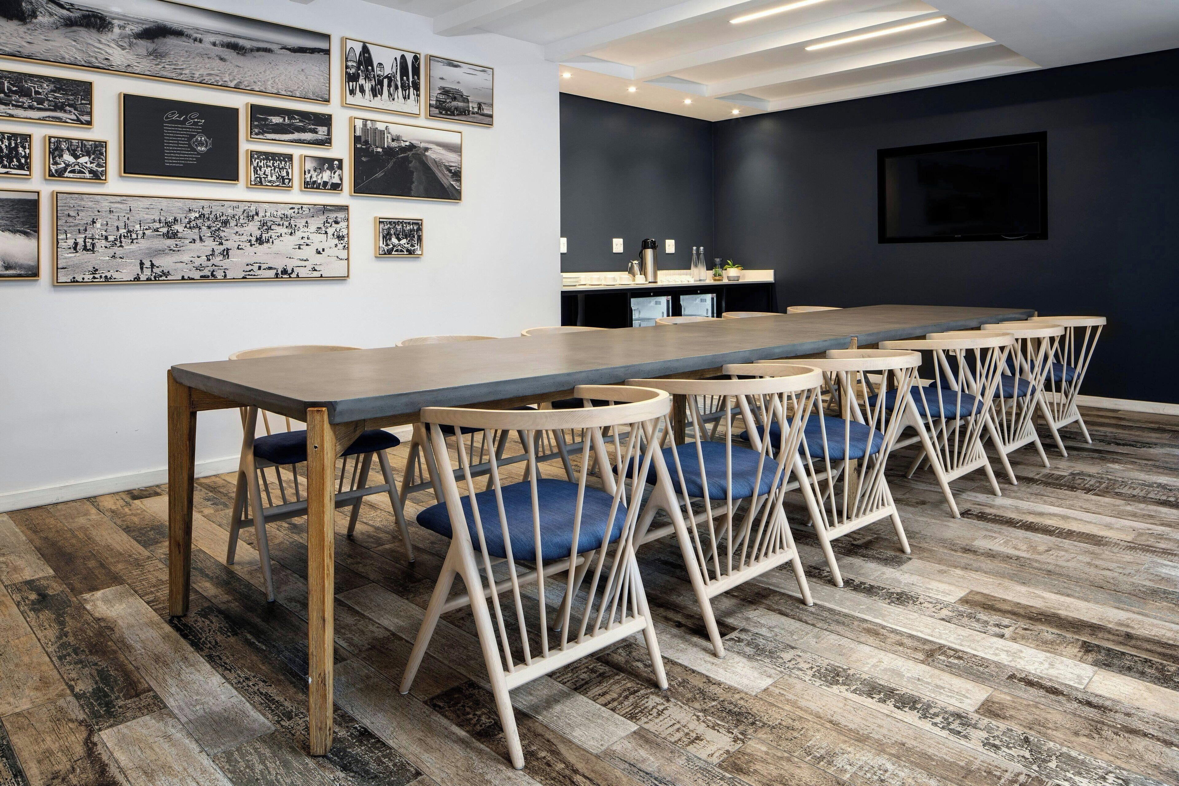 A conference room with a long table, chairs, and a dark wall with framed pictures.
