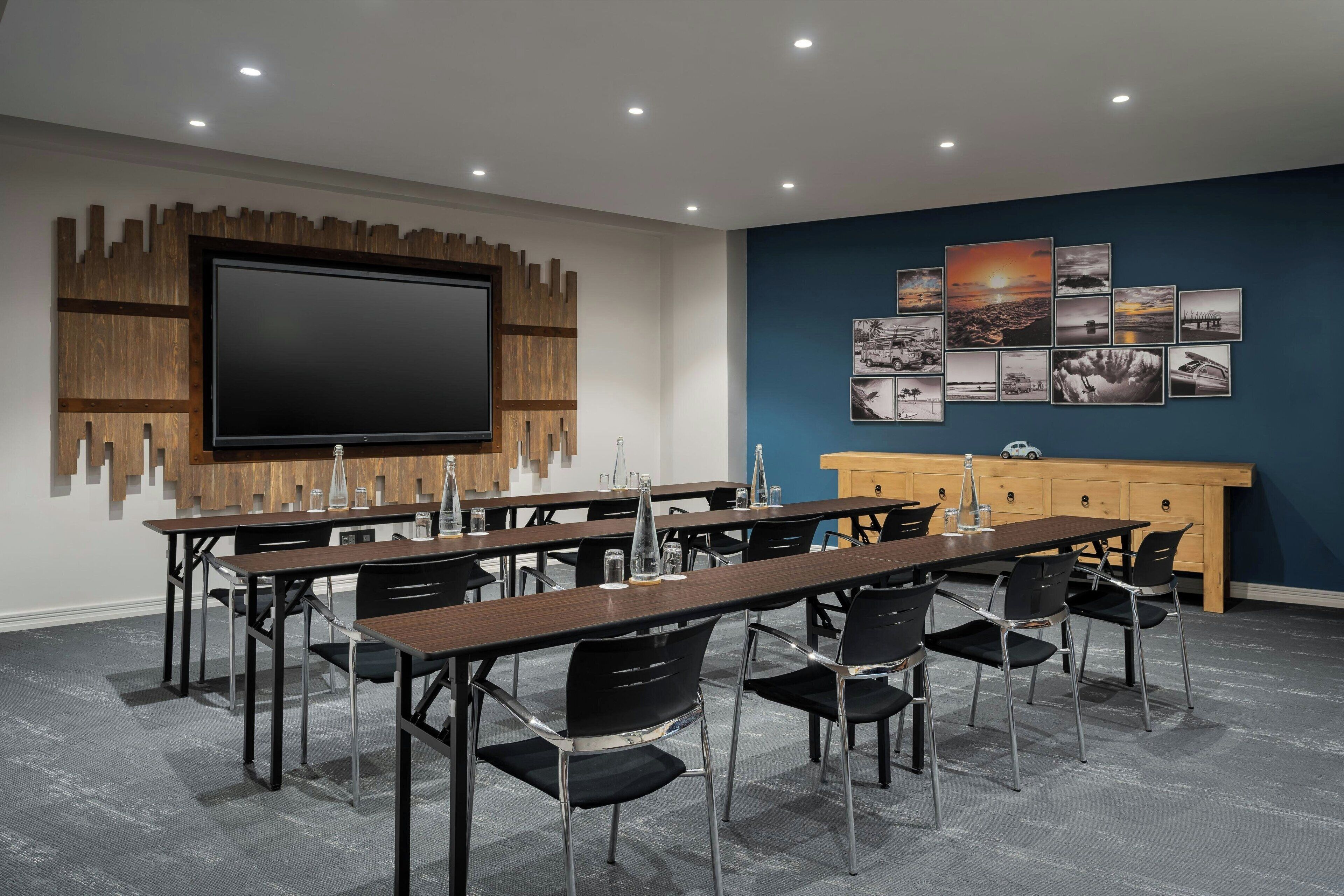 A conference room with a large flat-screen TV, a wooden panel wall, and a blue accent wall with framed pictures.
