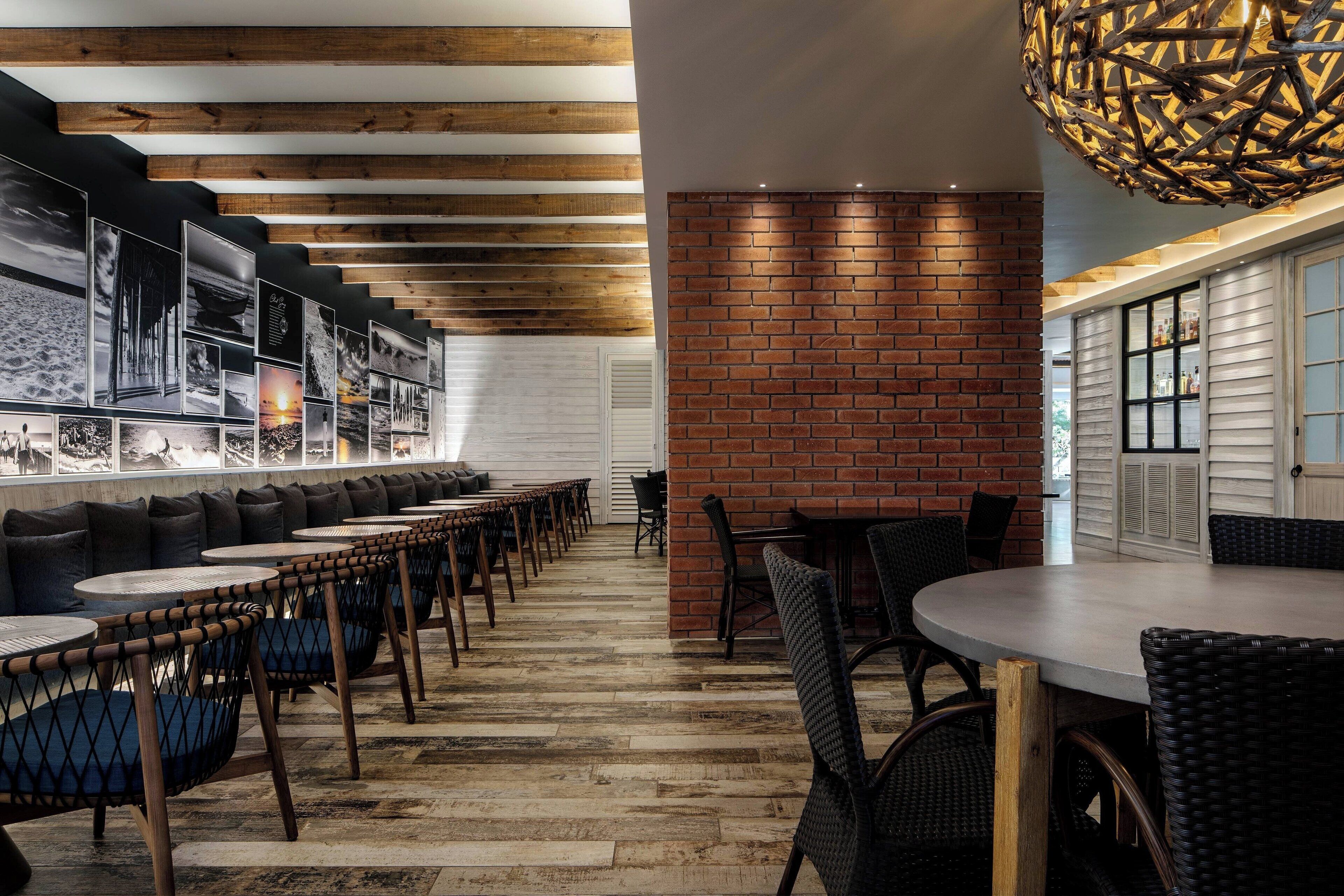 A modern restaurant with a long counter, cushioned seating, and a brick accent wall.
