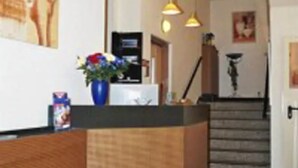 Zona d'acollida amb una taula de recepció de fusta, un ram de flors i una escala al fons.