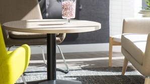 Um interior moderno com uma mesa redonda, uma cadeira amarela, um sofá bege e um vaso decorativo.