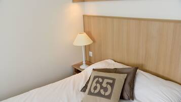 A neatly made bed with a pillow featuring the number 65, a bedside lamp, and a wooden headboard.