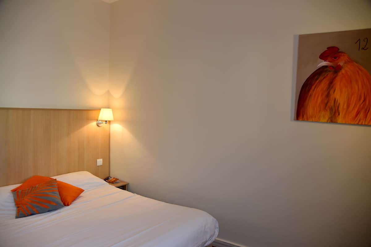 Una habitación de hotel con una cama, una mesita de noche, una lámpara y un cuadro en la pared.