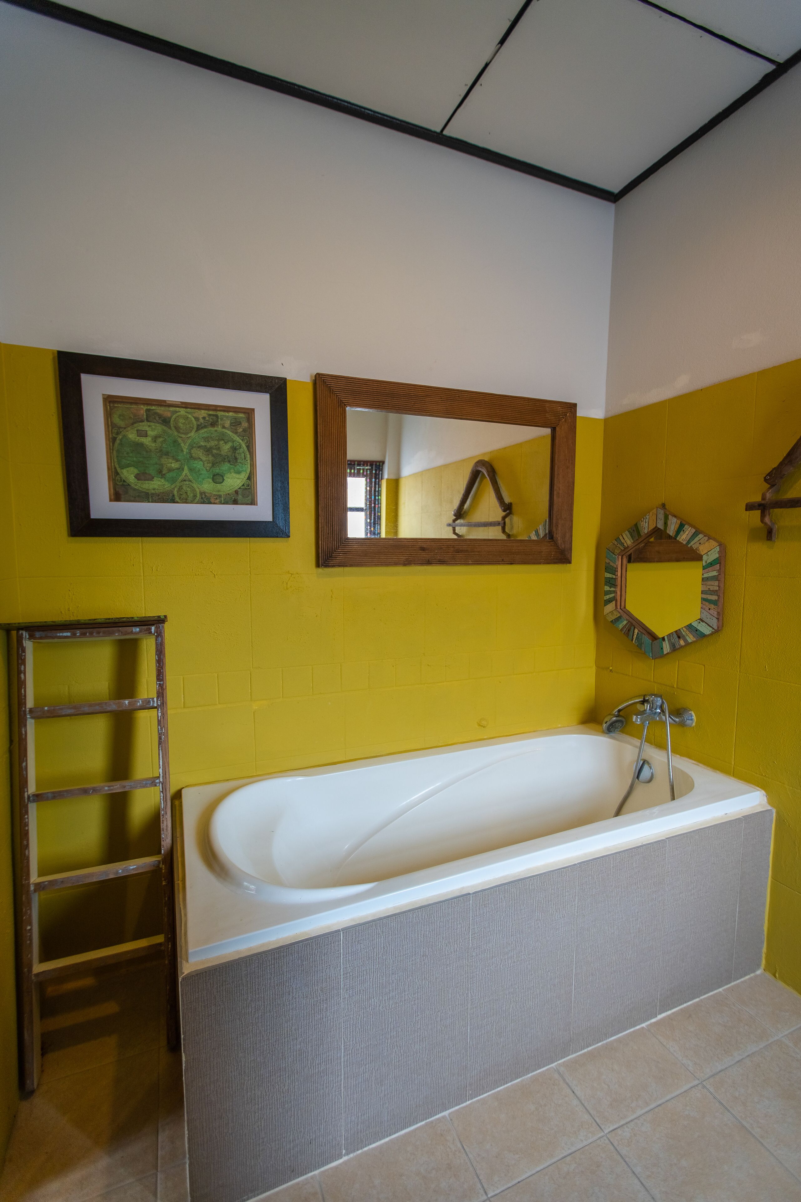 Une salle de bain avec une baignoire, une échelle en bois et deux miroirs au mur.
