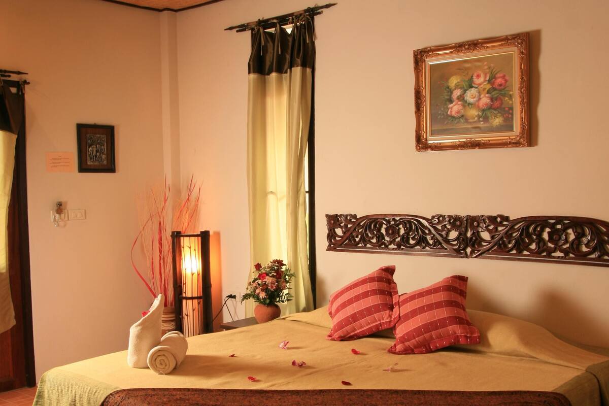 Ein ordentlich bezogenes Bett mit Blumenarrangement, einem gerahmten Bild an der Wand und einem dekorativen Kopfteil.