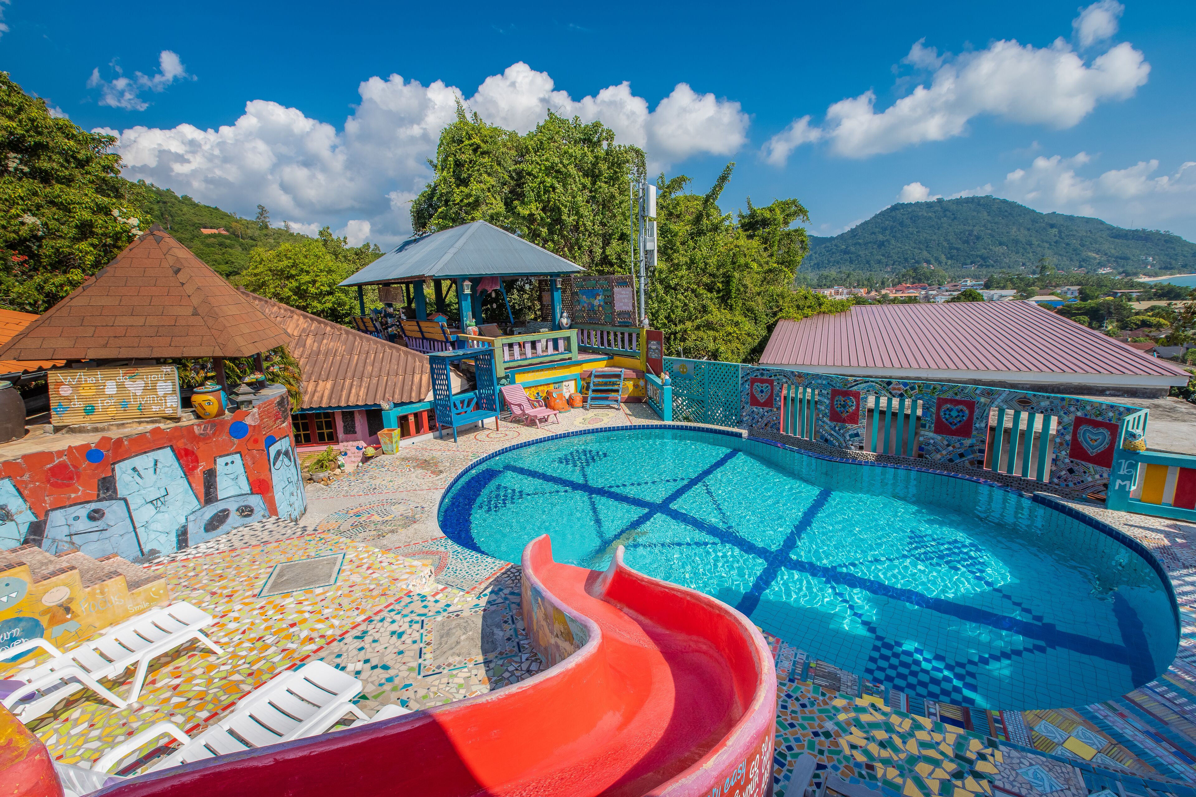 Un área de piscina colorida con un tobogán, sillas de descanso y un pabellón.