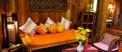 Una habitación con una cama de madera, almohadas coloridas, una mesita con un jarrón de flores y una silla con un cojín estampado.