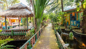 A wooden pathway leading to a thatched-roof structure surrounded by lush greenery and a small pond with decorative fish. - Varinda Garden Resort (Koh Samui)