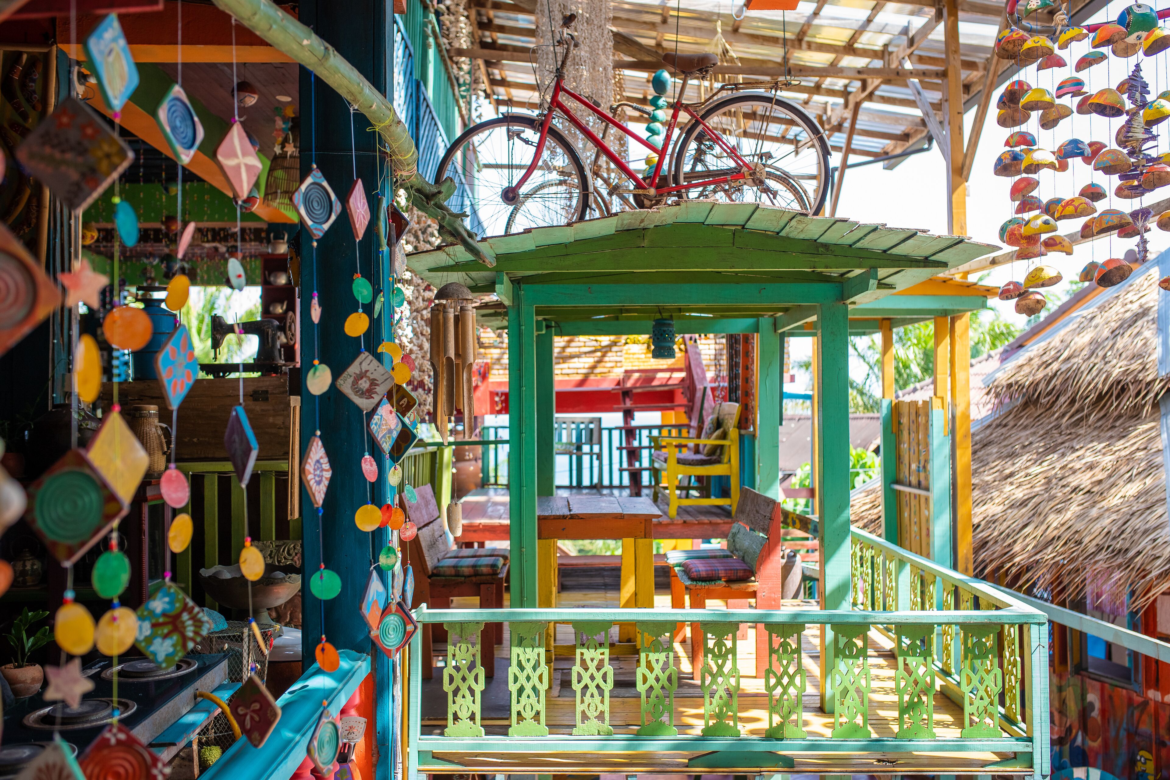 A colorful outdoor seating area with a thatched roof, a bicycle, and various hanging decorations.