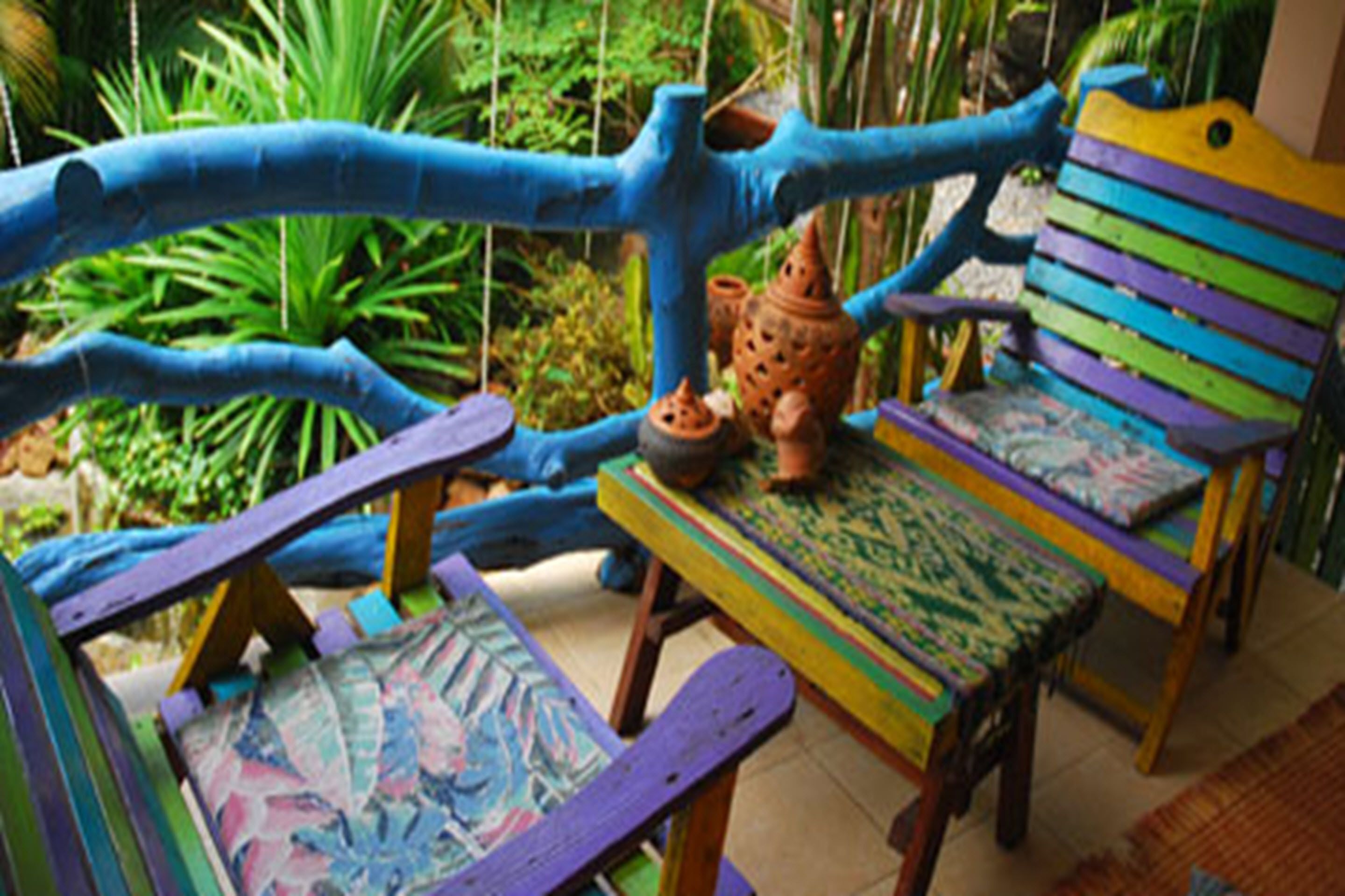 Un espace extérieur accueillant, agrémenté de mobilier coloré, avec une chaise bleue et violette, une petite table recouverte d’une nappe à motifs et un pot rustique.