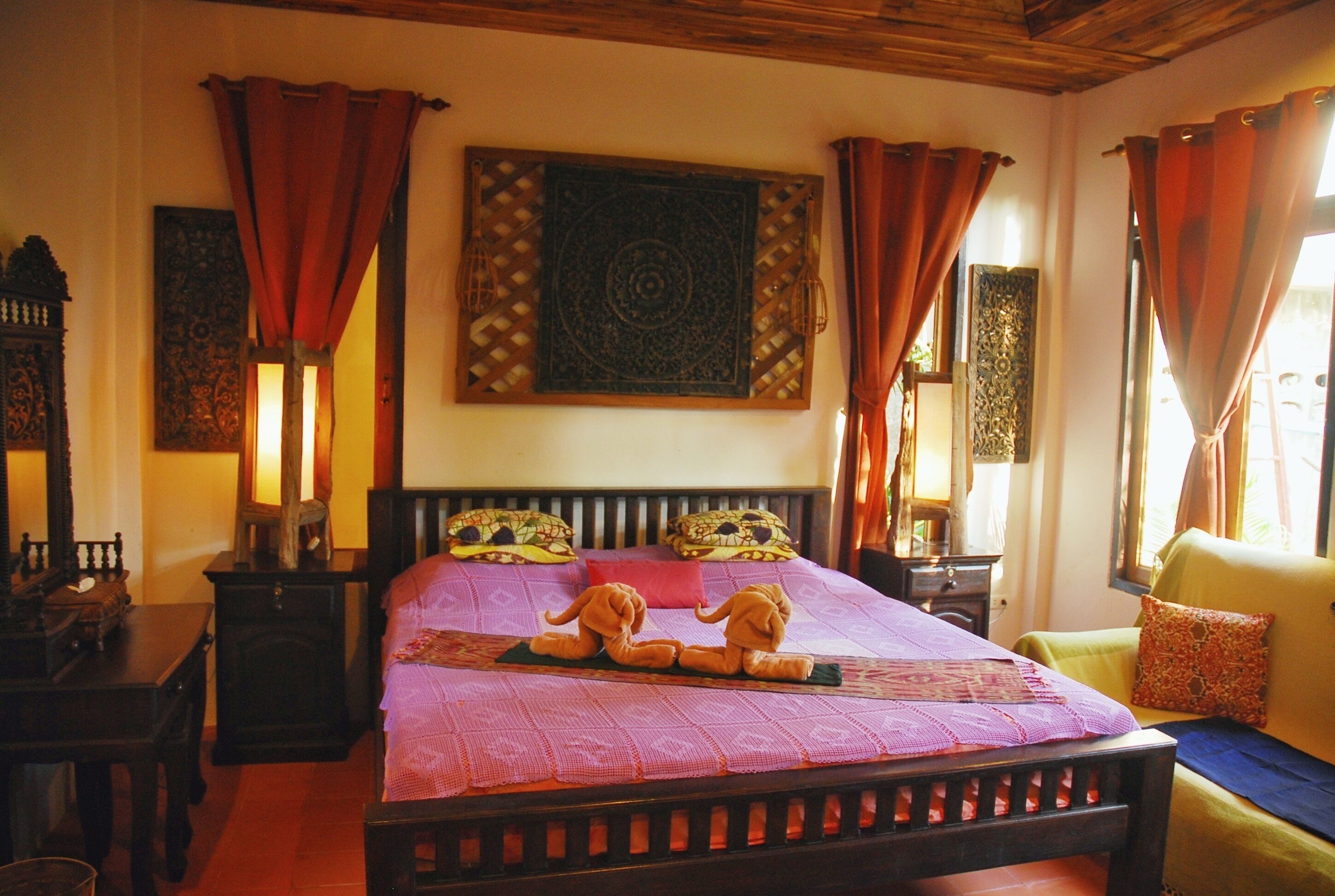 Une chambre à coucher avec un lit, une tête de lit en bois, des coussins décoratifs, une table de chevet et des rideaux.