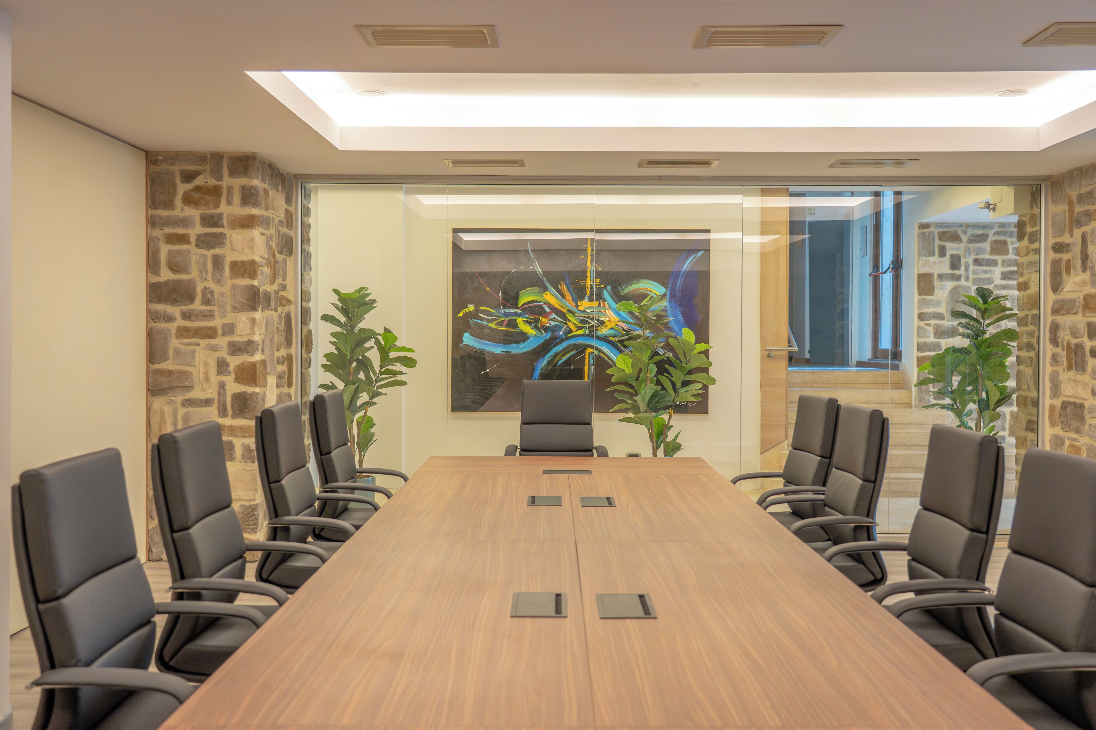 A conference room with a long table, black chairs, stone walls, and a modern abstract painting.