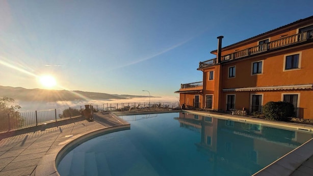 Una piscina con vistas despejadas al mar, un edificio con balcones y un atardecer al fondo.