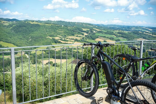 Un vélo garé sur un balcon, offrant une vue panoramique sur des collines et des champs vallonnés.