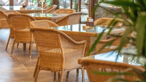 Un interior de restaurante con mobiliario de mimbre, mesas de cristal y vistas amplias a través de grandes ventanales.