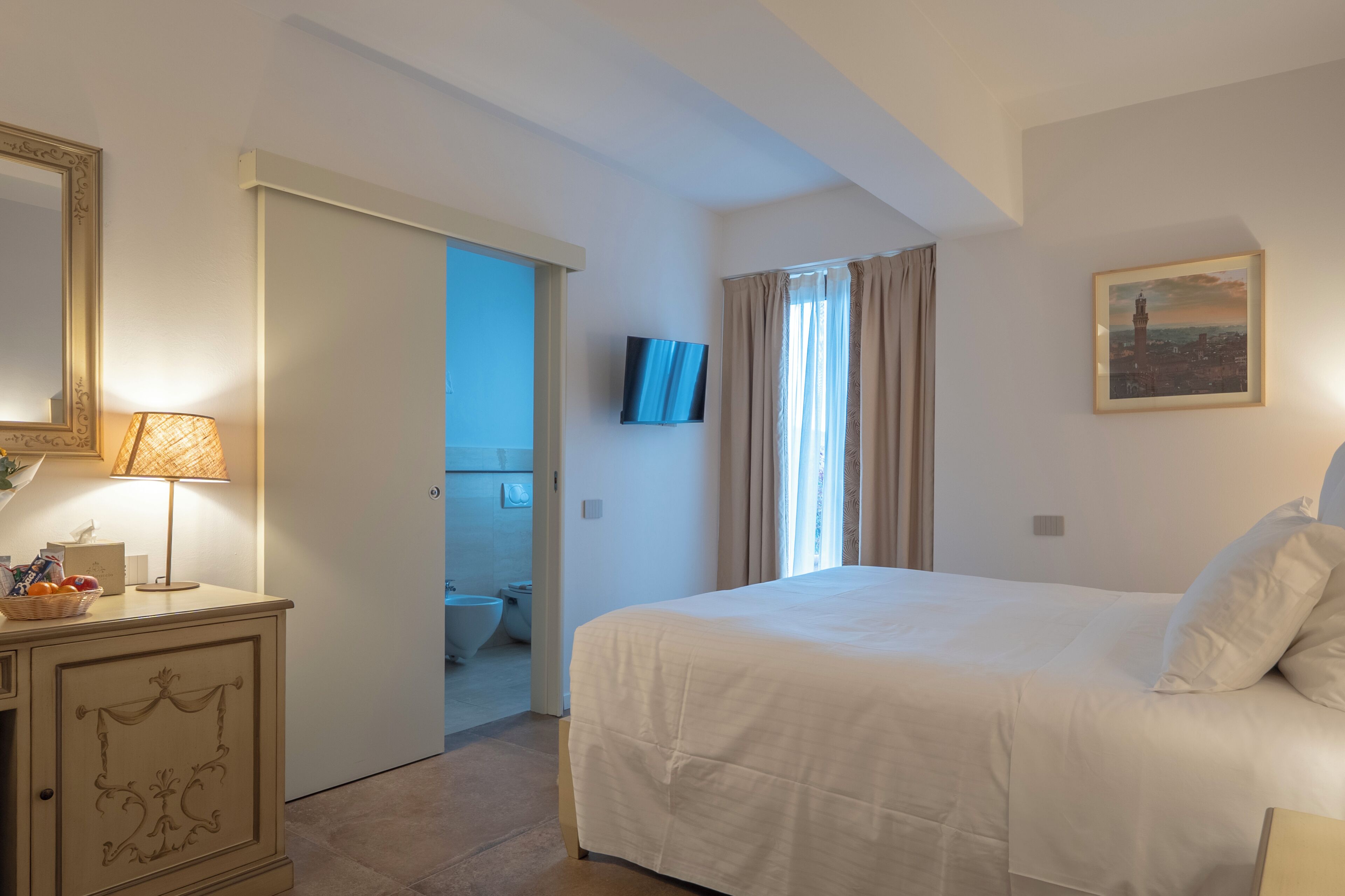 A hotel room with a bed, a television, a bathroom, and a door leading to another room.