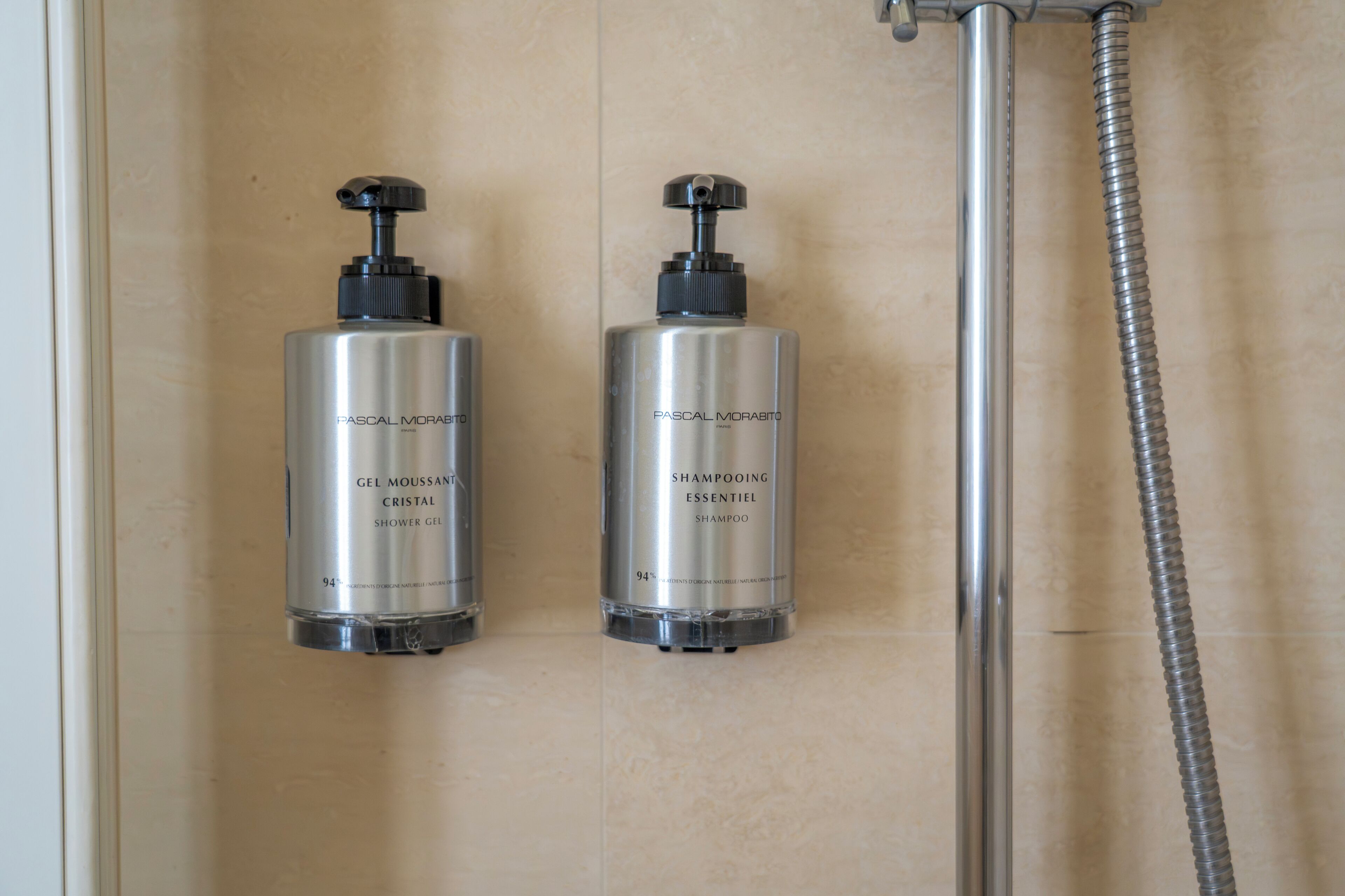 Dos botellas de gel de ducha con la etiqueta 'PASCAL MORABITO' en un baño con cabezal de ducha y manguera.