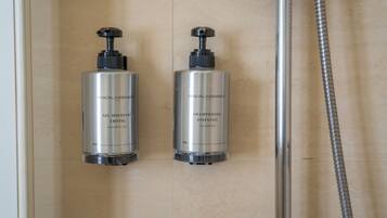 Dos botellas de gel de ducha con la etiqueta 'PASCAL MORABITO' en un baño con cabezal de ducha y manguera.
