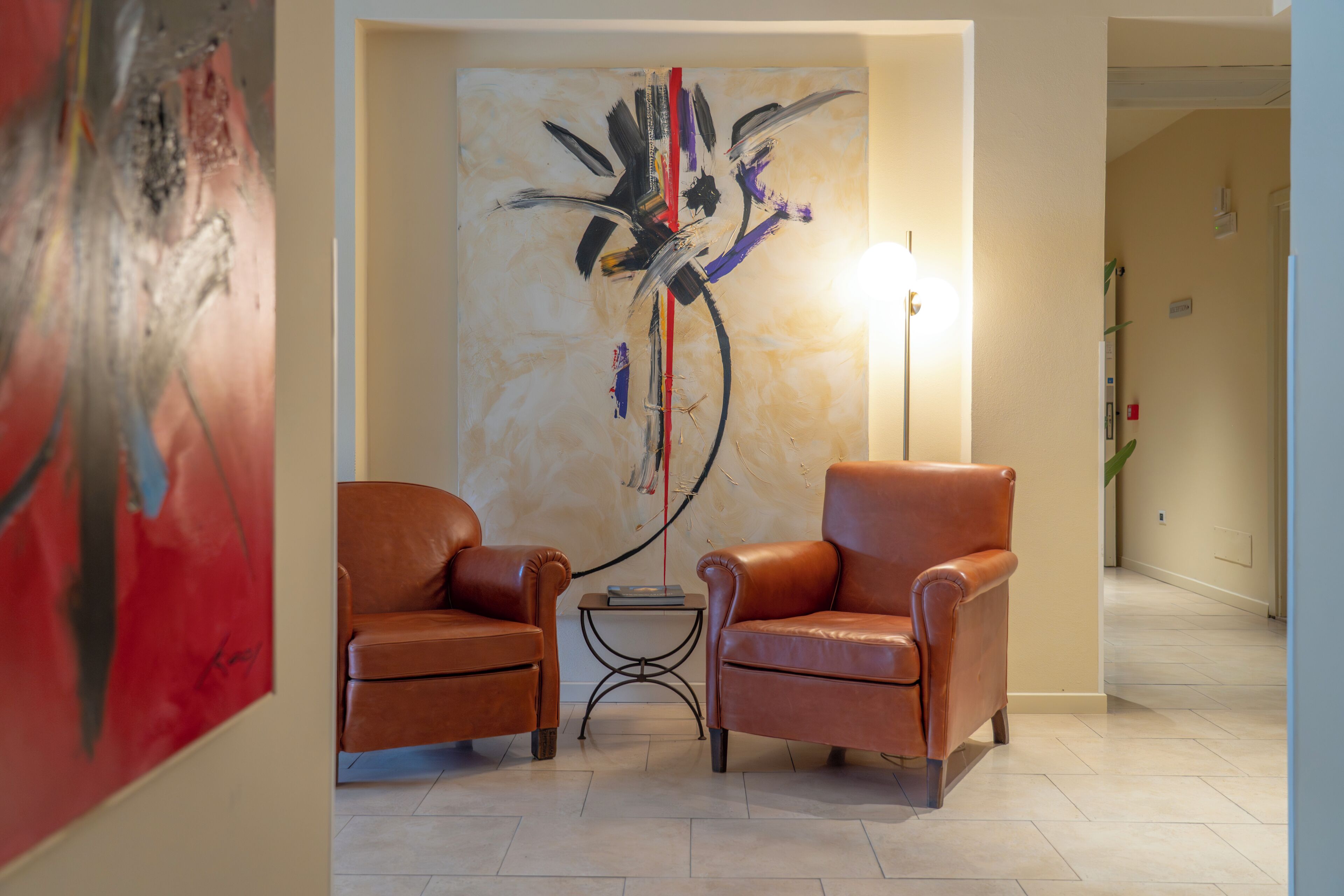 Een ontvangsthal met twee lederen fauteuils, een bijzettafeltje en een groot abstract schilderij aan de muur.