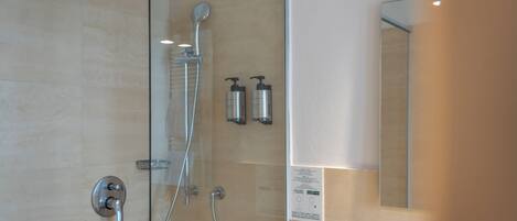 A modern bathroom with a glass shower enclosure, a handheld showerhead, and two bottles of shampoo.