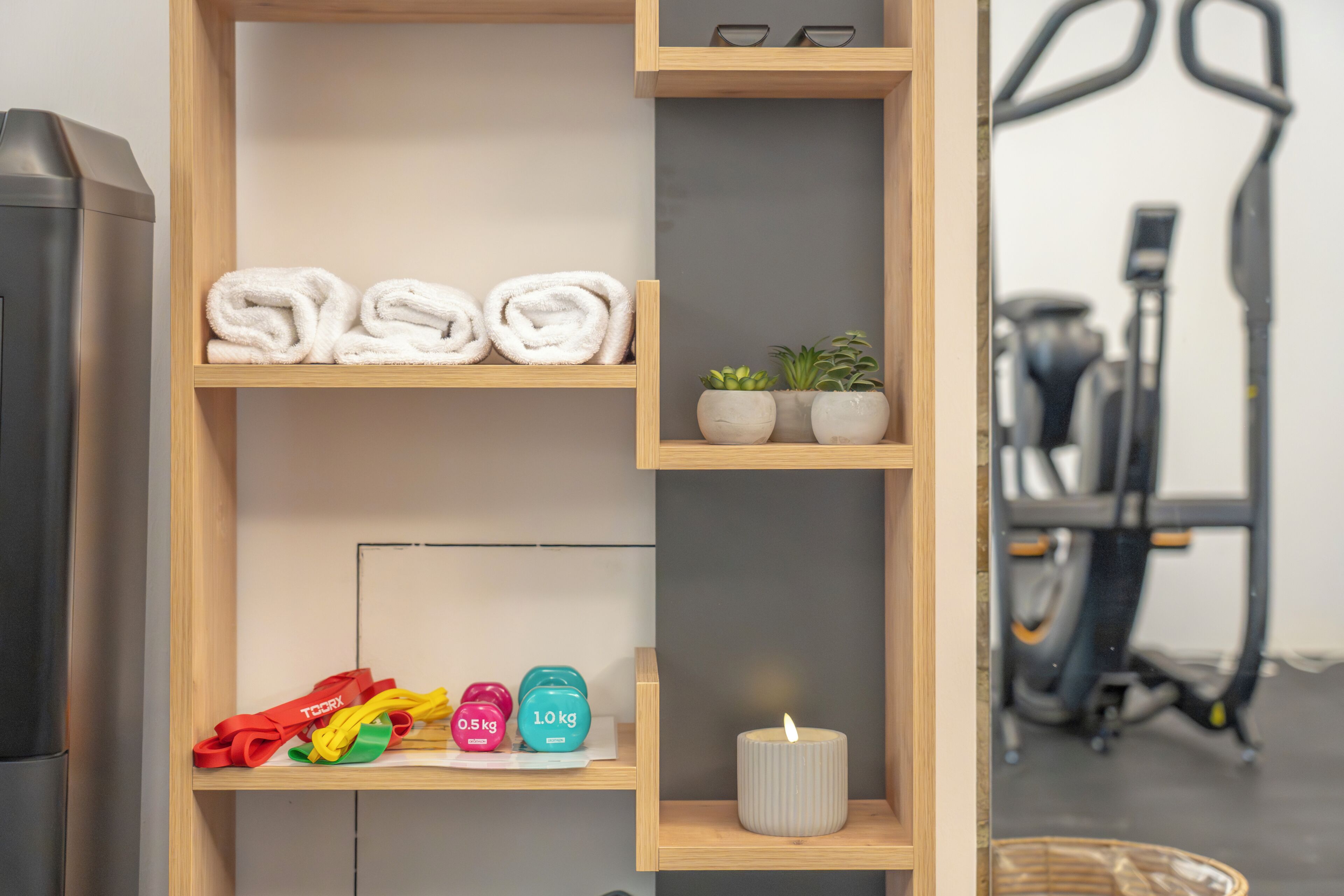 A wooden shelf with folded towels, small potted plants, resistance bands, and a candle.