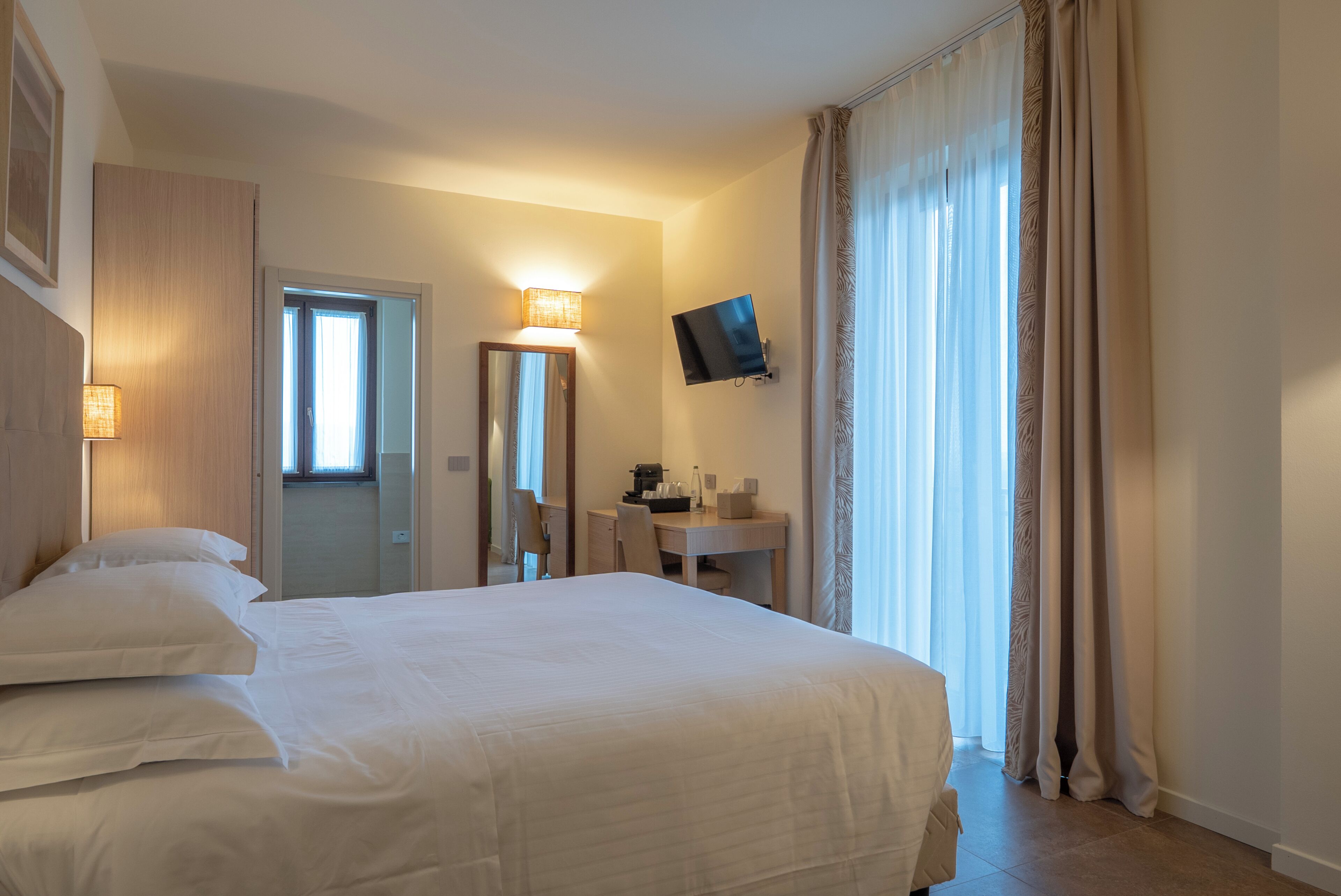 Ein Hotelzimmer mit Bett, Schreibtisch, Stuhl, Fernseher und Tür.