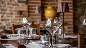 A dining table set with wine glasses, plates, and cutlery, with a brick wall and a vase in the background.