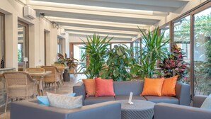 Un área de estar moderna con asientos, plantas en macetas y ventanas amplias.