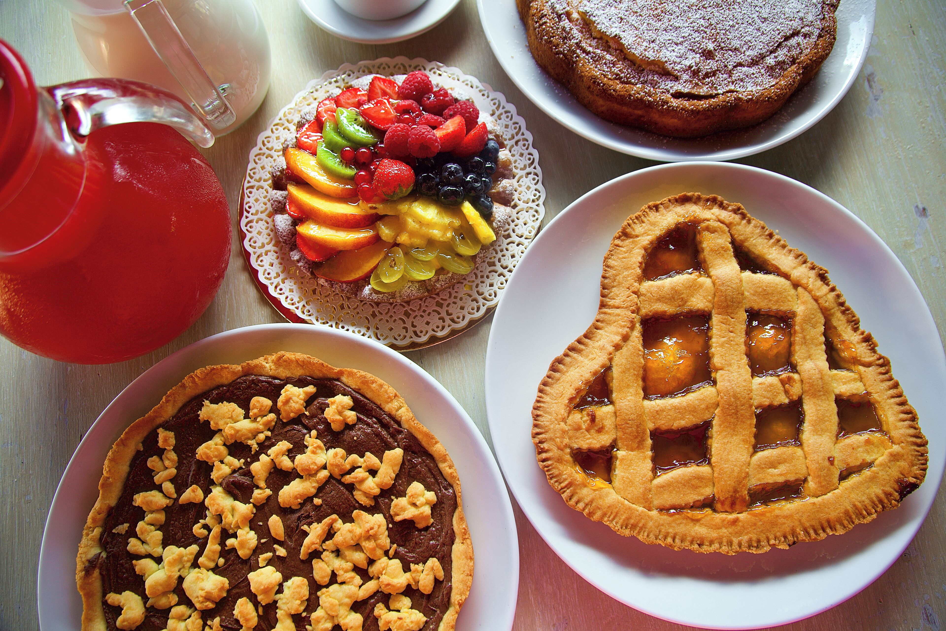 Et bord med forskellige desserter, heriblandt en frugttærte, en tærte med gittermønster og en chokoladedessert med nødder.